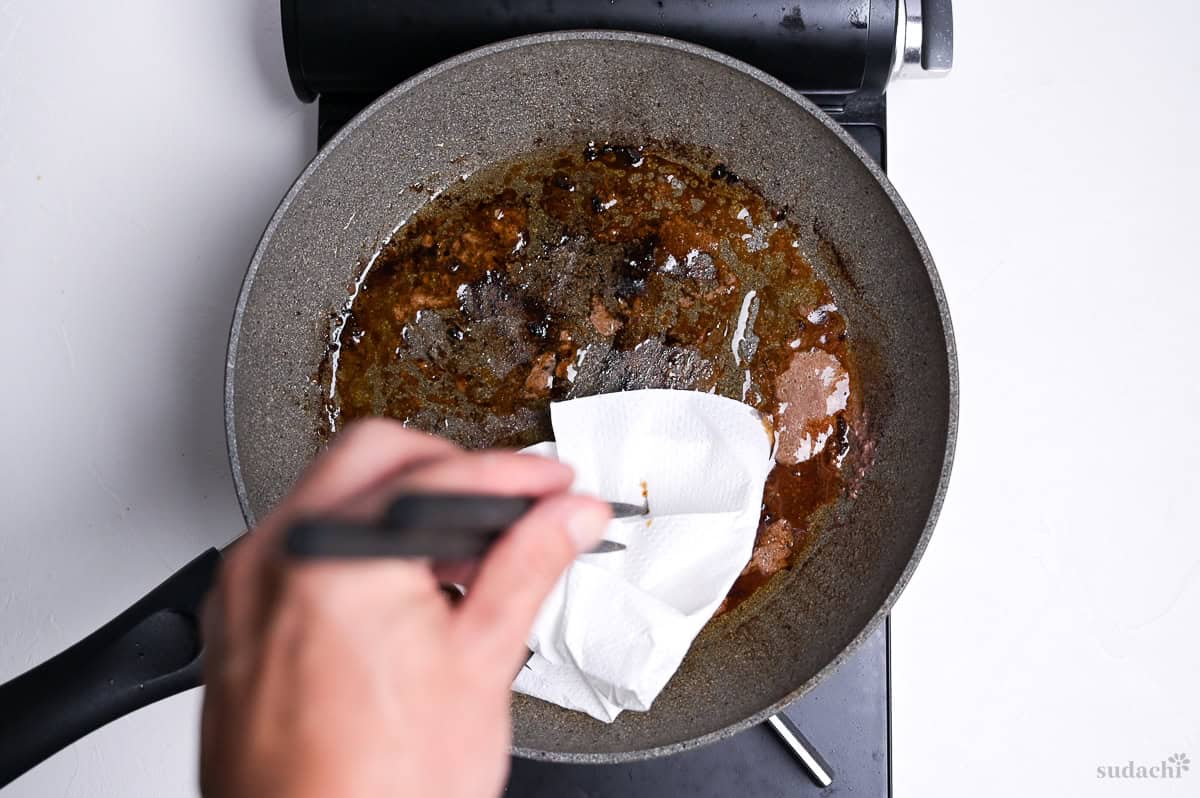 wiping out excess oil from cooking wafu hamburg from a frying pan with kitchen paper