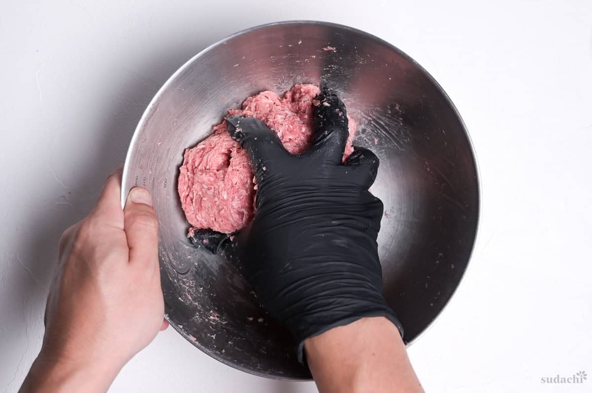 a gloved hand kneading ground meat to make wafu hamburg patties