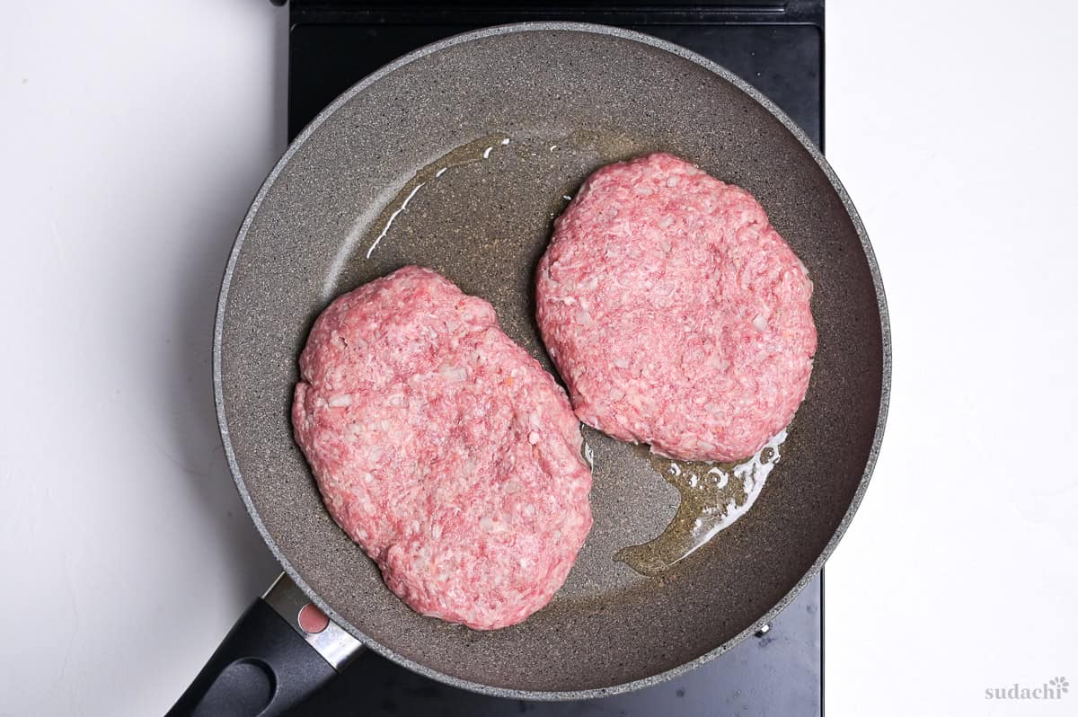 two homemade wafu hamburg patties placed in a frying pan on the stove top