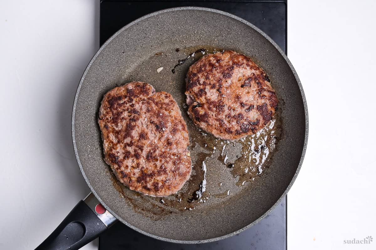 two wafu hamburgs frying in a pan on the stove top