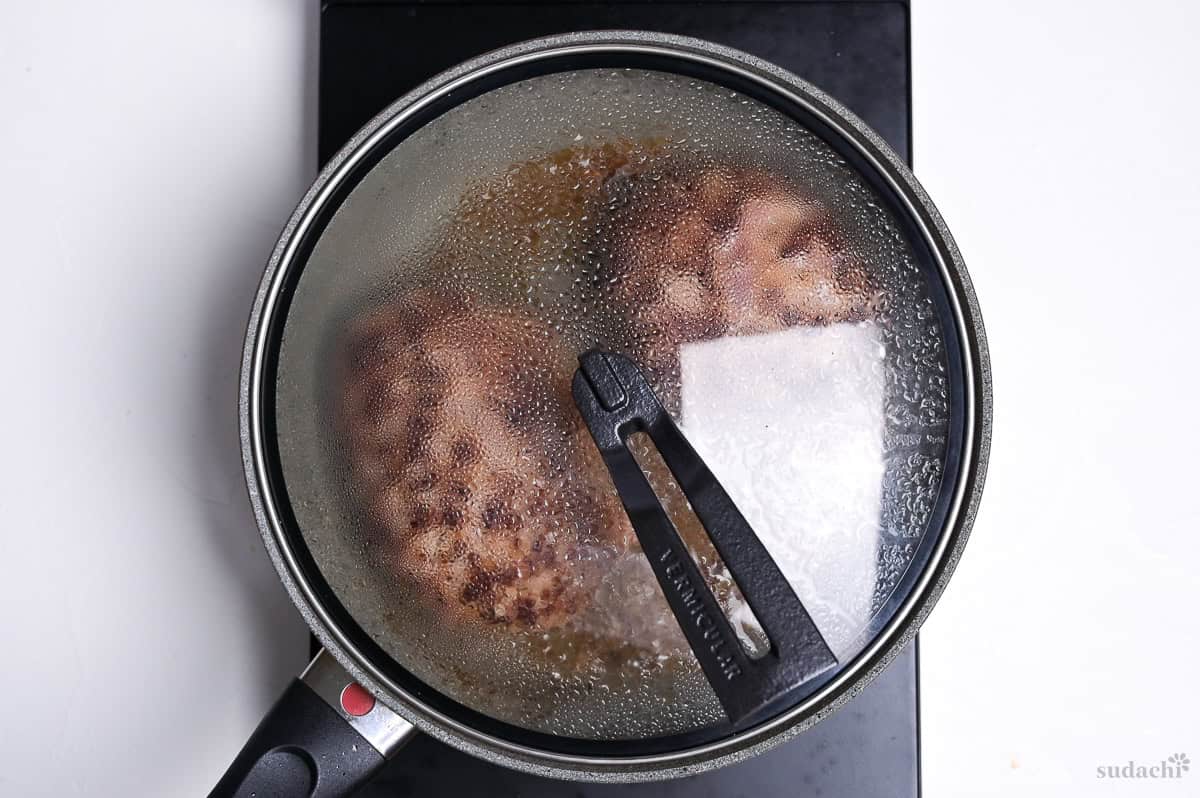 steam frying wafu hamburgs in a frying pan with lid on the stove top