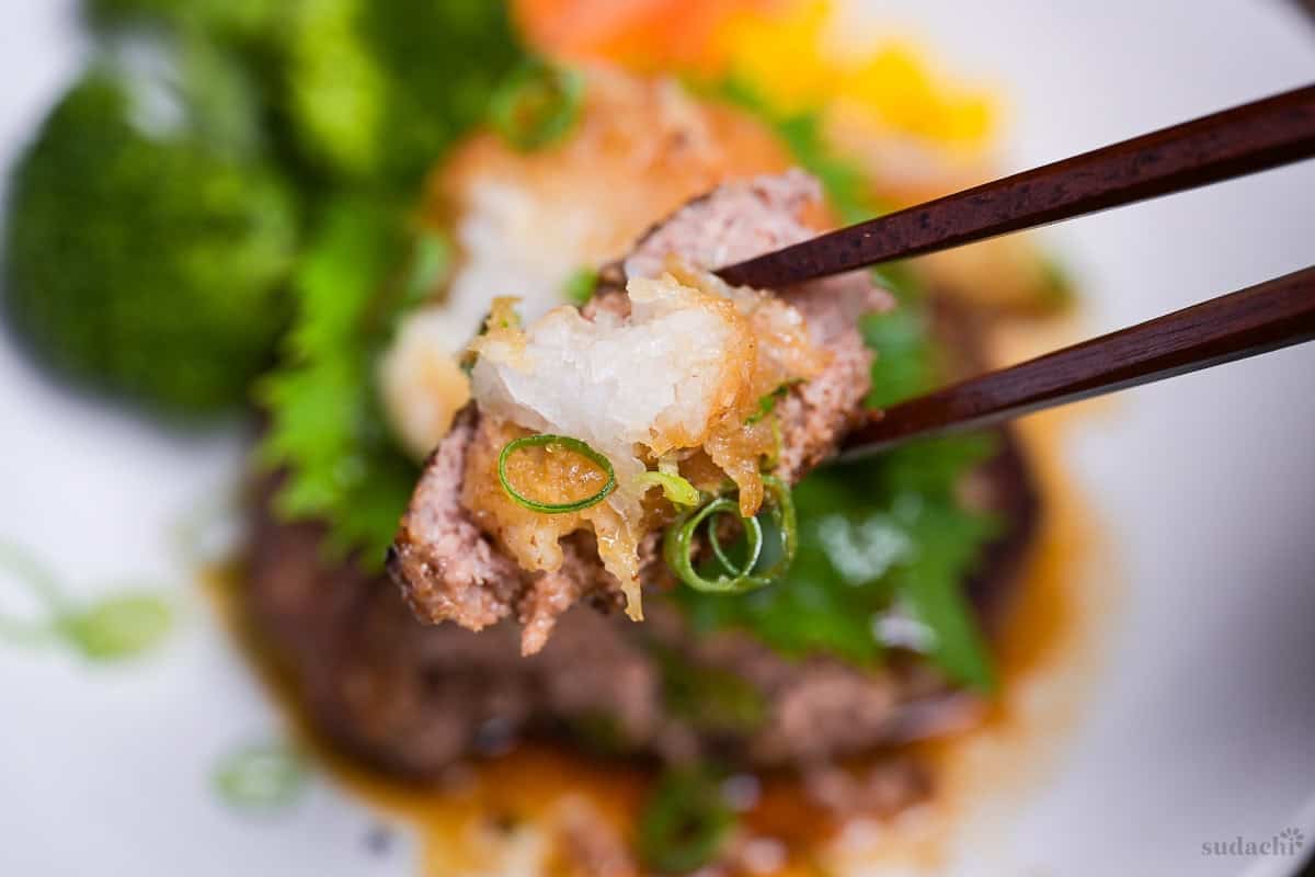 A piece of wafu hamburg with grated daikon held up with dark wooden chopsticks