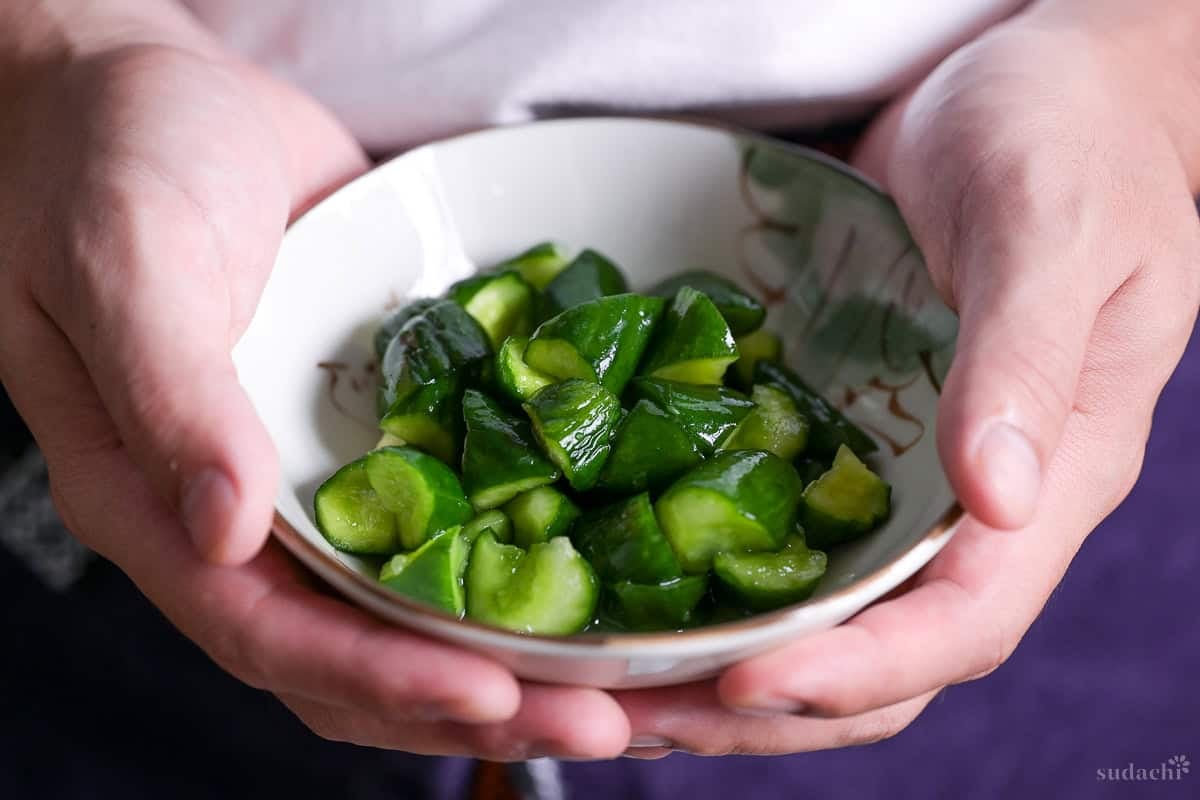Yuto Omura holding wasabi pickled cucumbers in a white bowl with brown rim