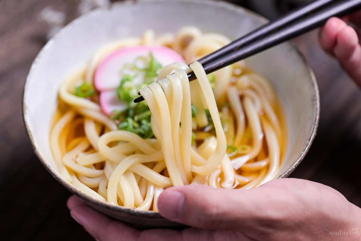 black chopsticks lifting udon out of a bowl of homemade kake udon noodle soup