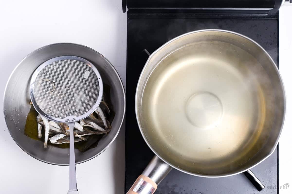 strained dashi in a pot on the stove top with niboshi and kombu in a bowl next to it
