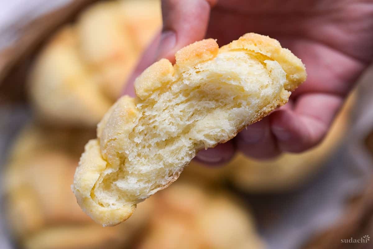A hand holding one half of a melon pan that has been torn to reveal pillowy soft bread inside