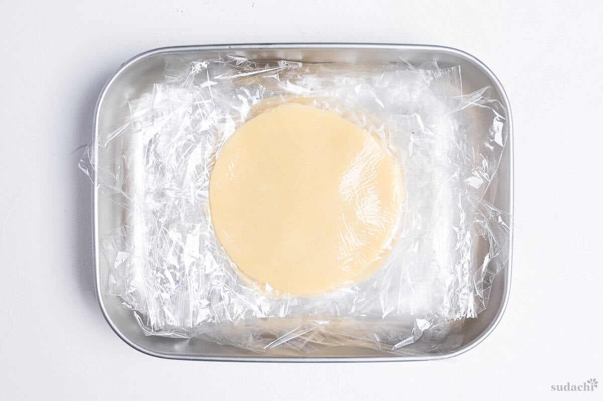 cookie dough for melon pan rolled into discs and stacked in a container with plastic wrap between them
