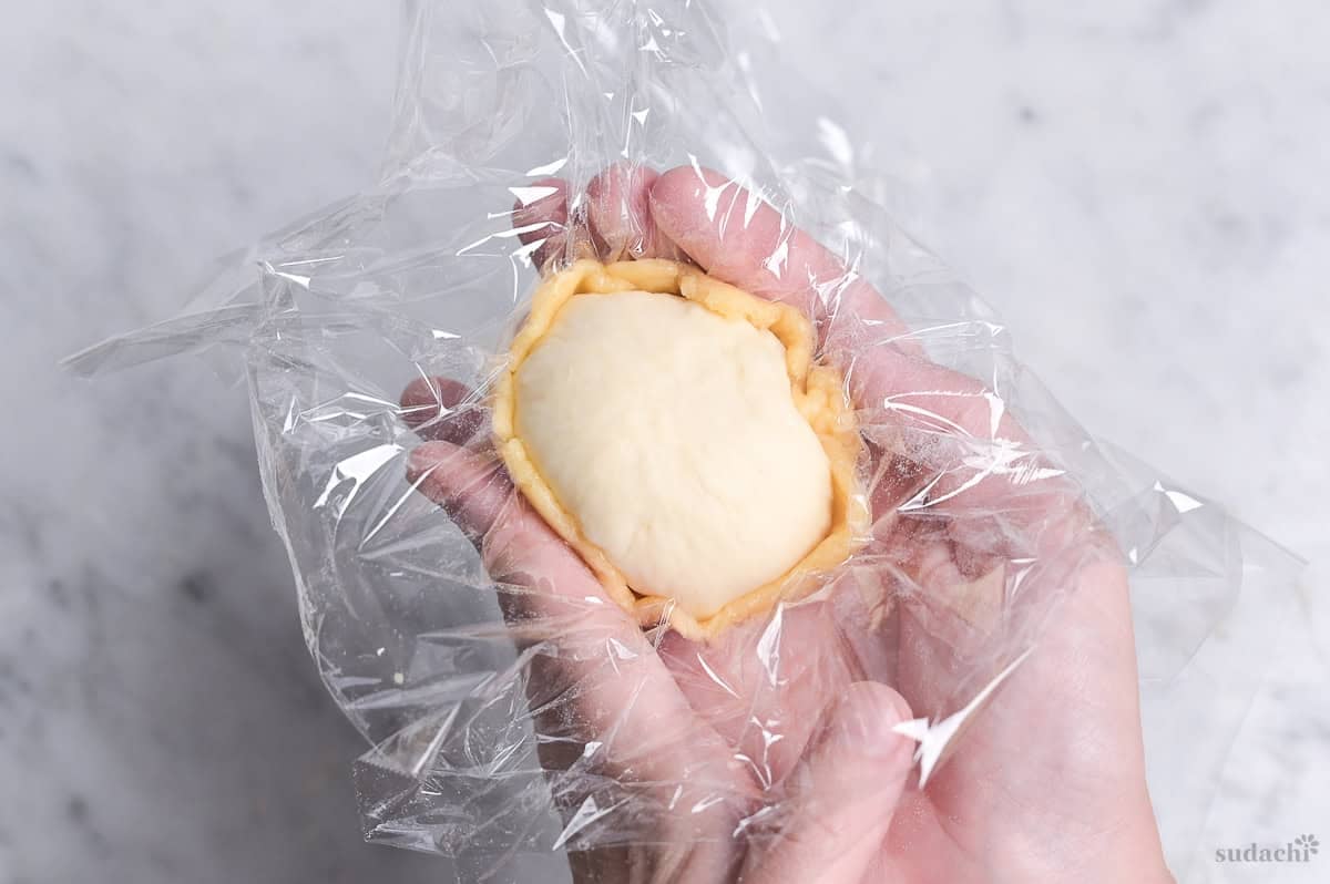 wrapping dough with cookie dough to shape melon pan