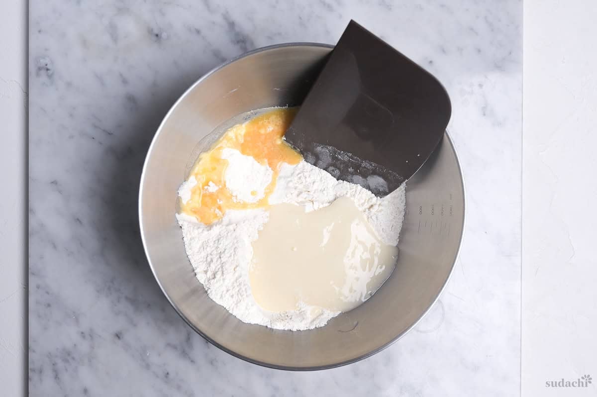 Mixing melon pan dough ingredients in a steel mixing bowl with plastic bench straper