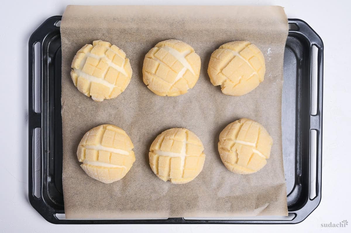 Melon pan with cracked cookie dough after final rise on a lined baking tray