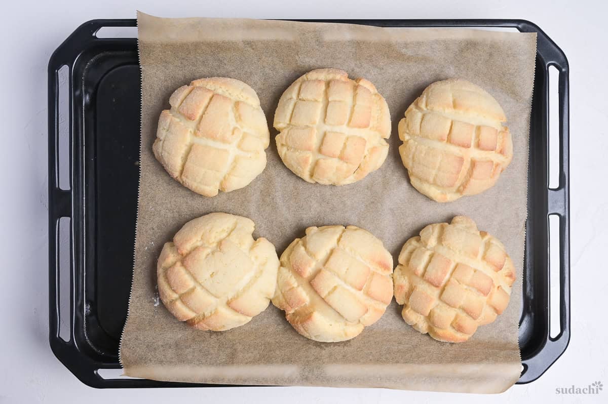 six baked melon pan on a baking sheet lined with brown parchment paper