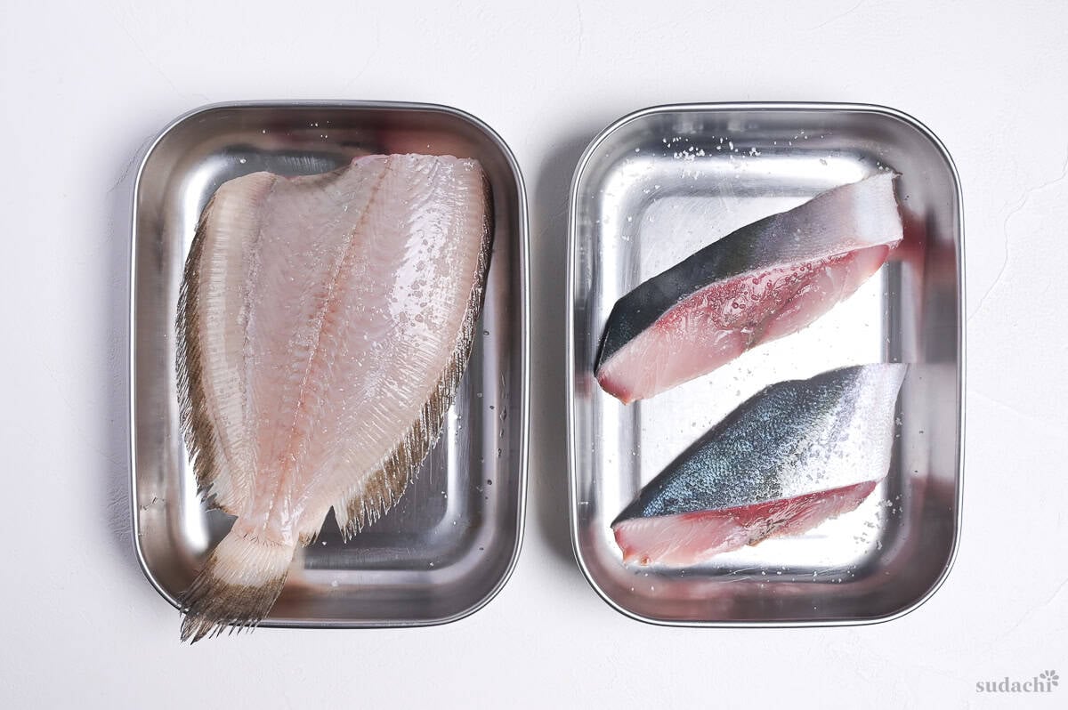 two steel containers side by side, flat fish fillet in the left one, two yellowtail fillets in the right one.