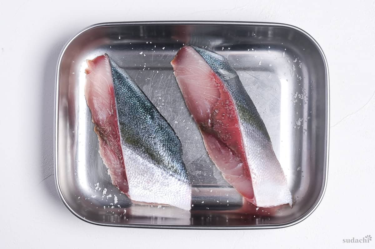 Two yellowtail fillets sprinkled with salt in a container