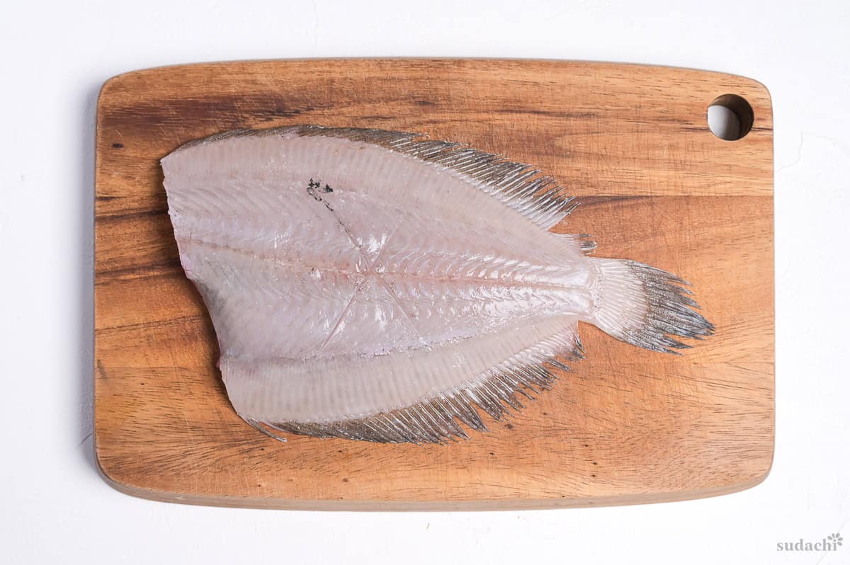 a cross scored on the surface of a flat fish fillet on a wooden cutting board