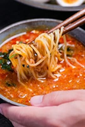 Wooden chopsticks holding ramen noodles in a bowl of spicy tsukemen ramen soup