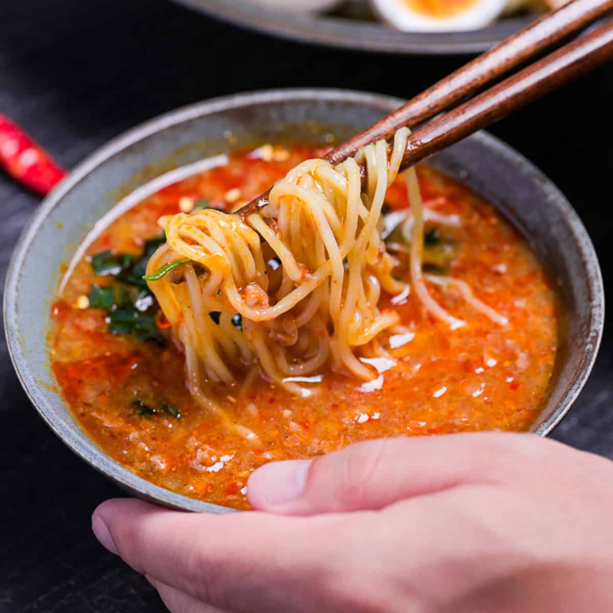 Wooden chopsticks holding ramen noodles in a bowl of spicy tsukemen ramen soup