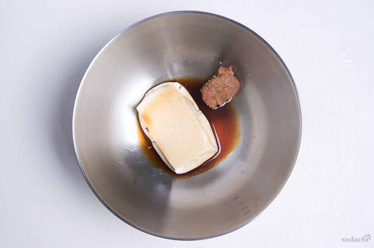 a small block of firm tofu in a bowl with miso and soy sauce.