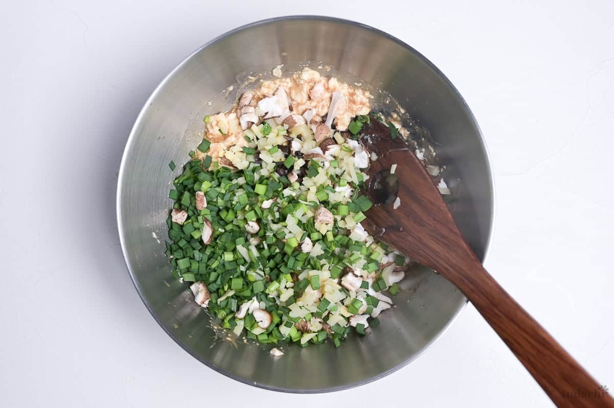 Tofu gyoza filling ingredients finely cut and placed in a bowl with wooden spatula.