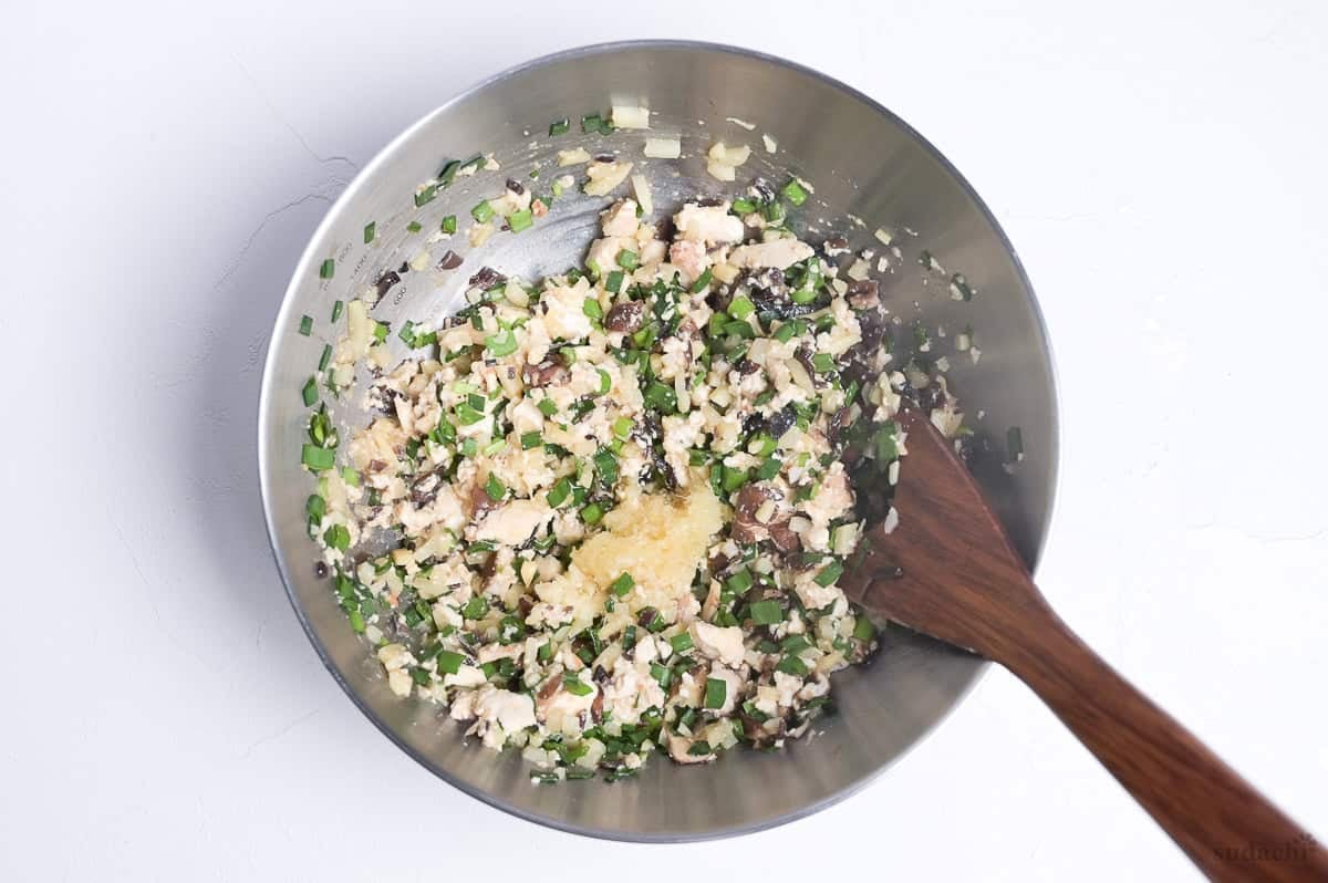 Tofu gyoza filling with grated ginger and garlic on top of the mixture in a bowl.