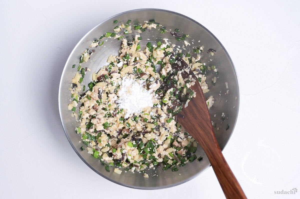 Cornstarch added to tofu gyoza filling in a steel mixing bowl.