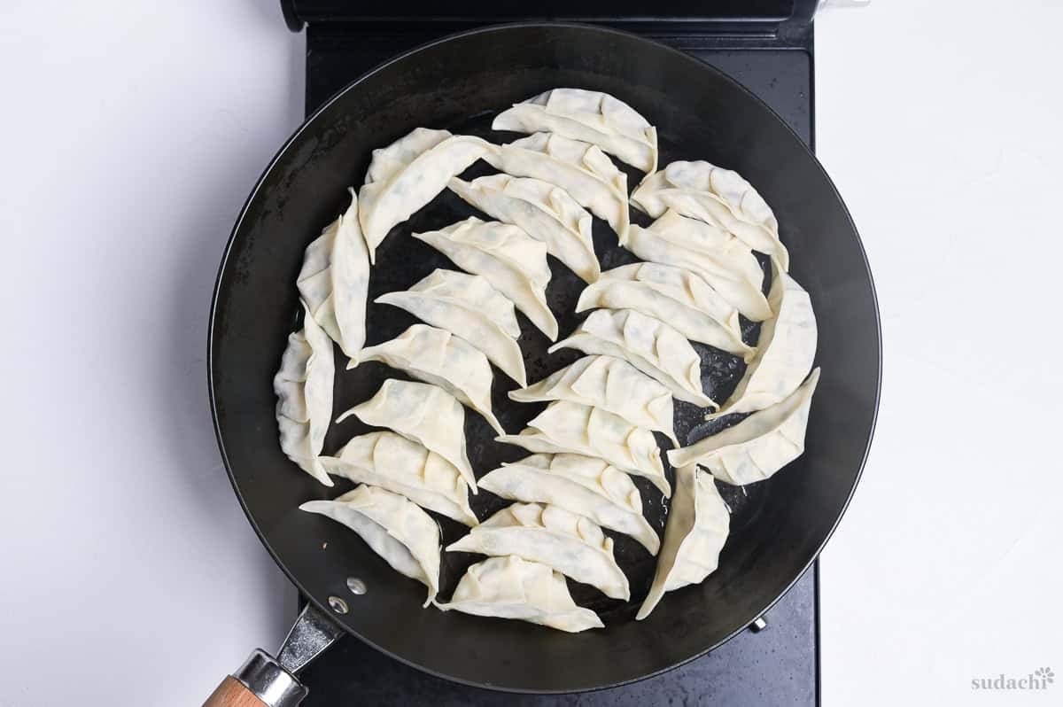 tofu gyoza arranged in a single layer in a frying pan on the stove top.