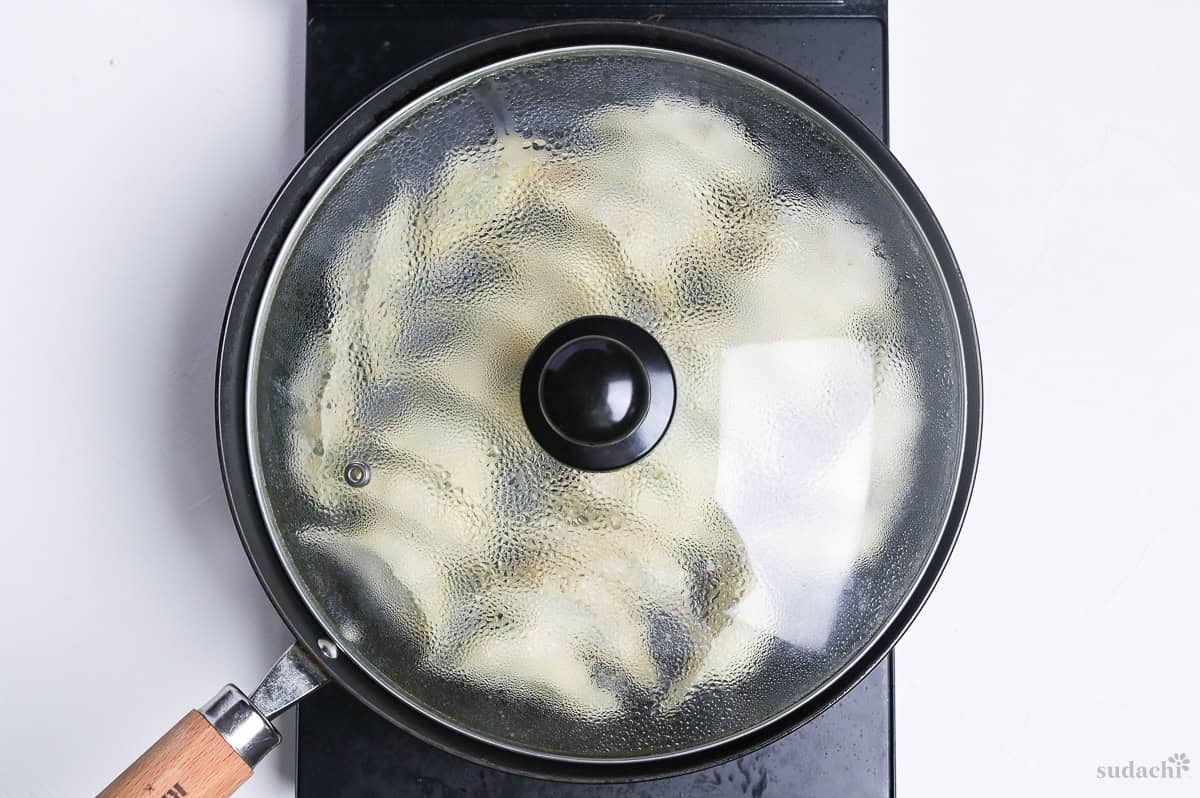 tofu gyoza cooking in a frying pan with lid (steam frying) on the stove top.
