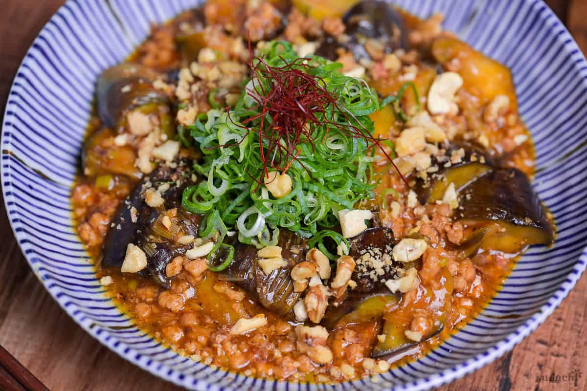Plant-based mabo nasu (mapo eggplant) topped with chopped green onion and chili threads served in a white dish with blue striped edge