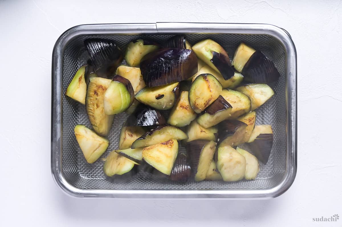 pan fried eggplant pieces in a mesh basket over a steel container
