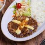 Bikkuri Donkey Inspired hamburg steak topped with a cross of melted cheese, next to white rice and salad served on a white oval plate thumbnail