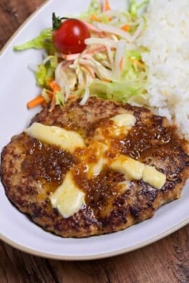 Bikkuri Donkey Inspired hamburg steak topped with a cross of melted cheese, next to white rice and salad served on a white oval plate thumbnail