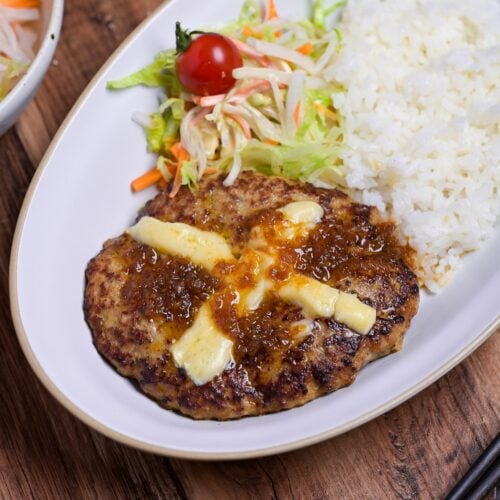 Bikkuri Donkey Inspired hamburg steak topped with a cross of melted cheese, next to white rice and salad served on a white oval plate thumbnail