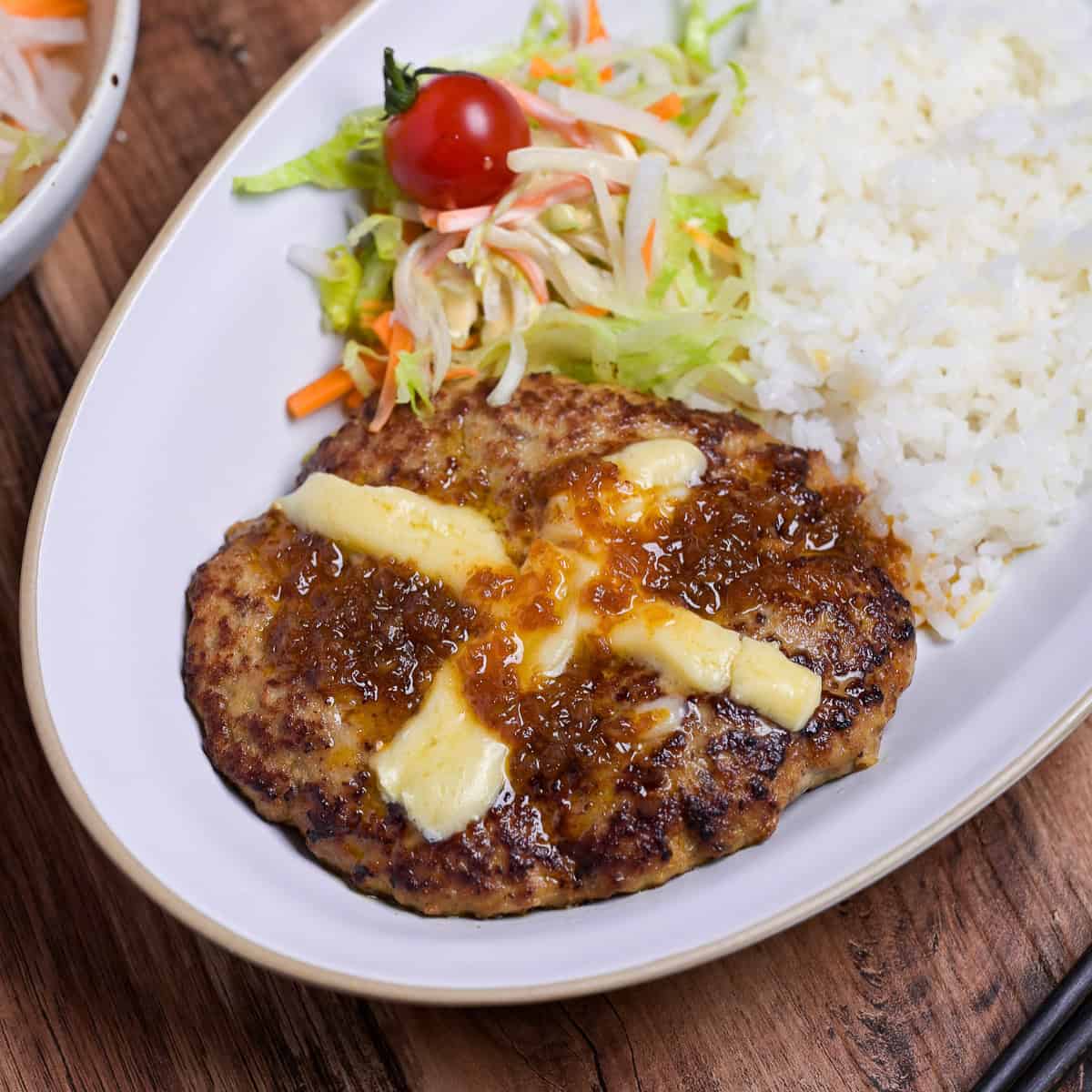 Bikkuri Donkey Inspired hamburg steak topped with a cross of melted cheese, next to white rice and salad served on a white oval plate thumbnail