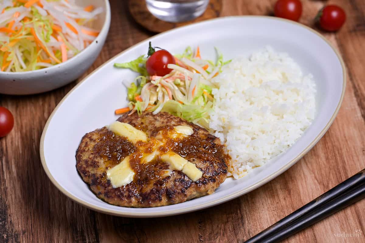 Bikkuri Donkey Inspired hamburg steak topped with a cross of melted cheese, next to white rice and salad served on a white oval plate