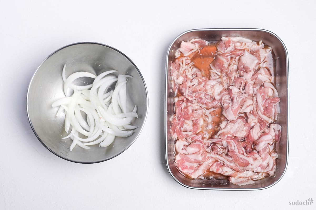 thinly sliced onion, salted in a bowl. Marinated thinly sliced pork belly in a steel rectangular container. (Prep for pork udon noodle soup)