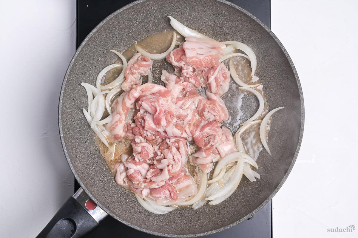 thinly sliced pork belly and onions frying in a pan on the stove top