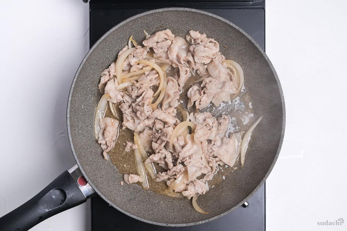 thinly sliced pork belly and onions frying in a pan on the stove top