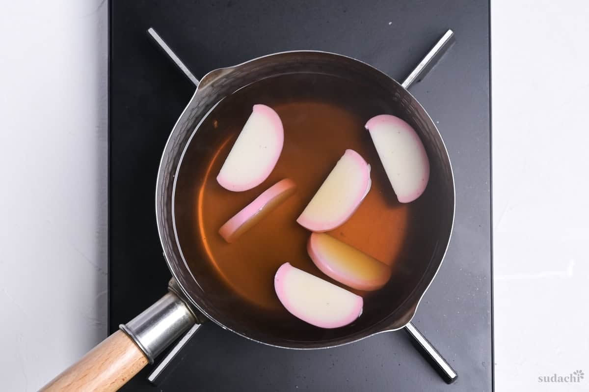 warming six slices kamaboko in a pot of udon noodle broth on the stove top