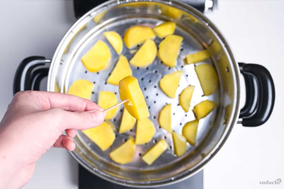 steamed sweet potato pieces in a steaming basket, with a pierced piece held above to show softness